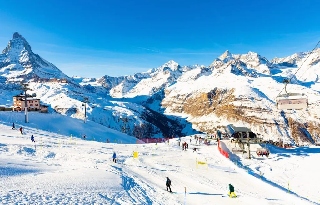 Malerische Berglandschaft mit dem hohen pyramidenförmigen Felsgipfel des Matterhorns in den Penninischen Alpen, bedeckt mit Schnee an einem sonnigen Wintertag, mit modernen Skiliften an seinem Fuß, Schweiz