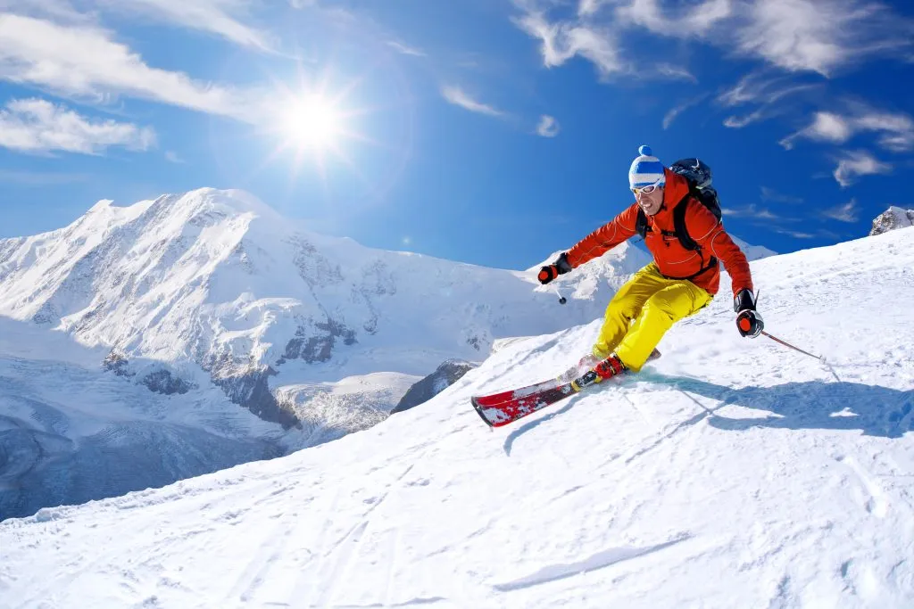 Skifahrer beim Abfahrtslauf im Hochgebirge vor blauem Himmel